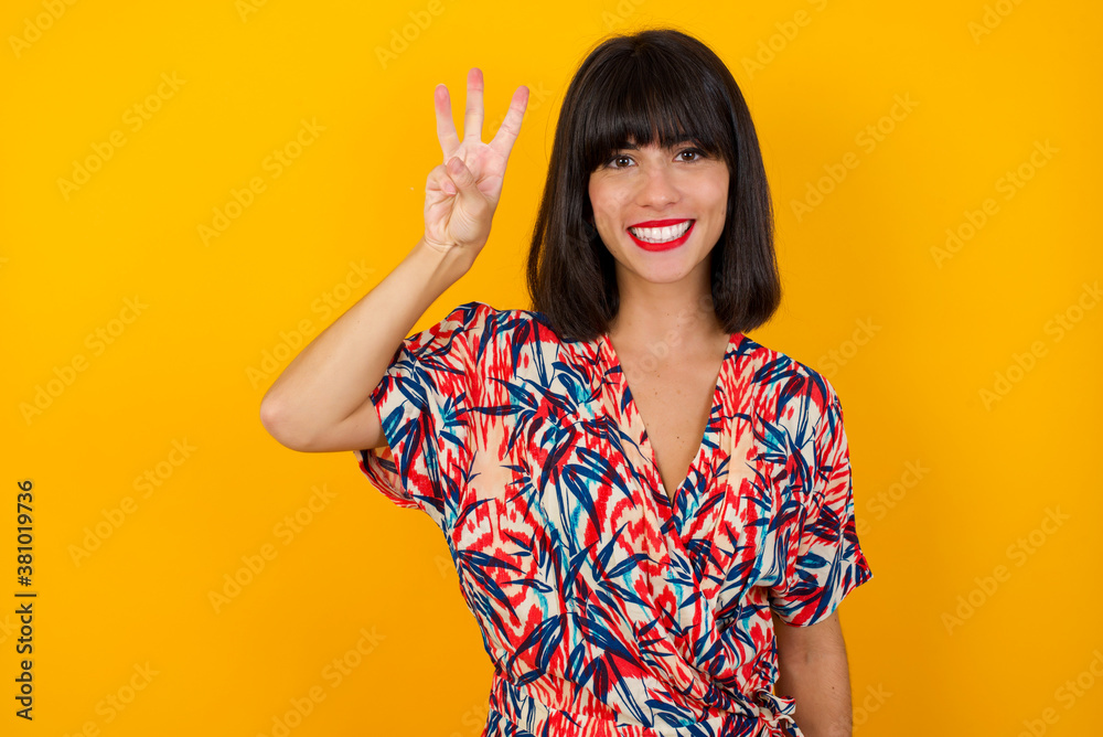 Young blonde woman standing standing against gray wall showing and pointing up with fingers number three while smiling confident and happy. Young blonde woman standing standing against gray wall showing and pointing up with fingers number three while smiling confident and happy.
