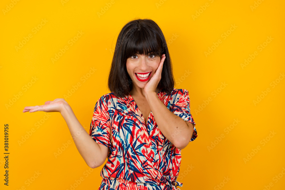 Positive glad female says: wow how exciting it is, has amazed expression, indicates something. Joyful pretty young woman demonstrates something. One hand on her head and pointing with other hand. Positive glad female says: wow how exciting it is, has amazed expression, indicates something. Joyful pretty young woman demonstrates something. One hand on her head and pointing with other hand.