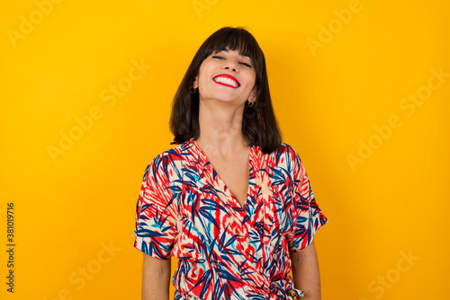 Beautiful smiling brunette female with broad smile, shows white teeth, wears casual t shirt, stands over gray studio wall rejoices having day off. Woman standing indoors.