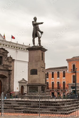 Quito, Ecuador - December 2, 2008: Historic Downtown. Plaza Santo Domingo. Statue of Jose de Sucre on pedestal in front of cathedral. People on square under gray cloudscape. photo