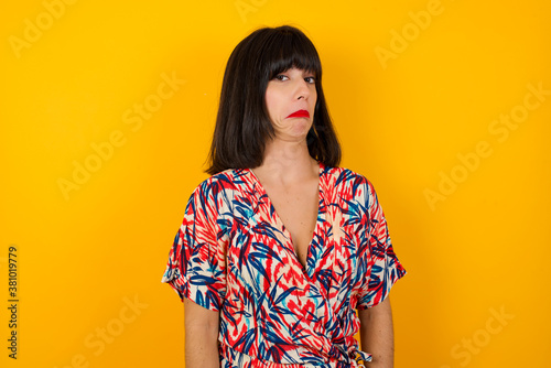 Beautiful woman with snobbish expression curving lips and raising eyebrows, looking with doubtful and skeptical expression, suspect and doubt. Standing indoors over gray background.