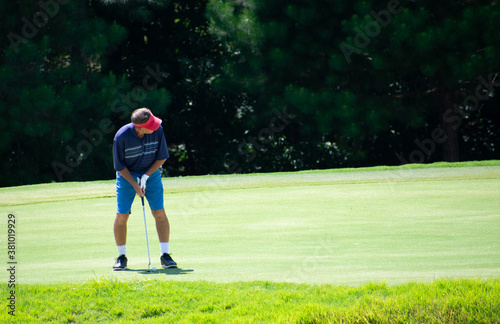 A man golfer putting a golf ball on a golf green with a pin at a golf course country club