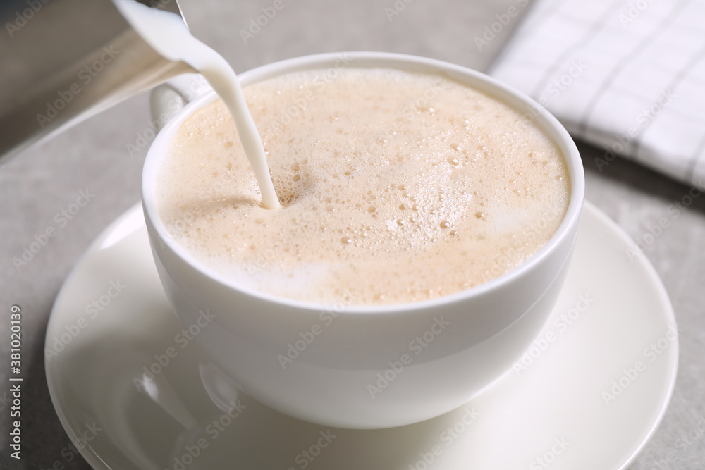Pouring milk into cup of coffee on grey table, closeup Pouring milk into cup of coffee on grey table, closeup