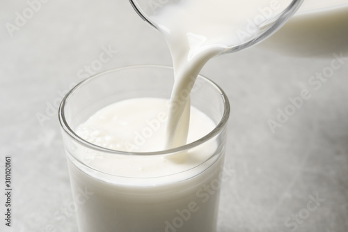 Pouring milk into glass on grey table, closeup