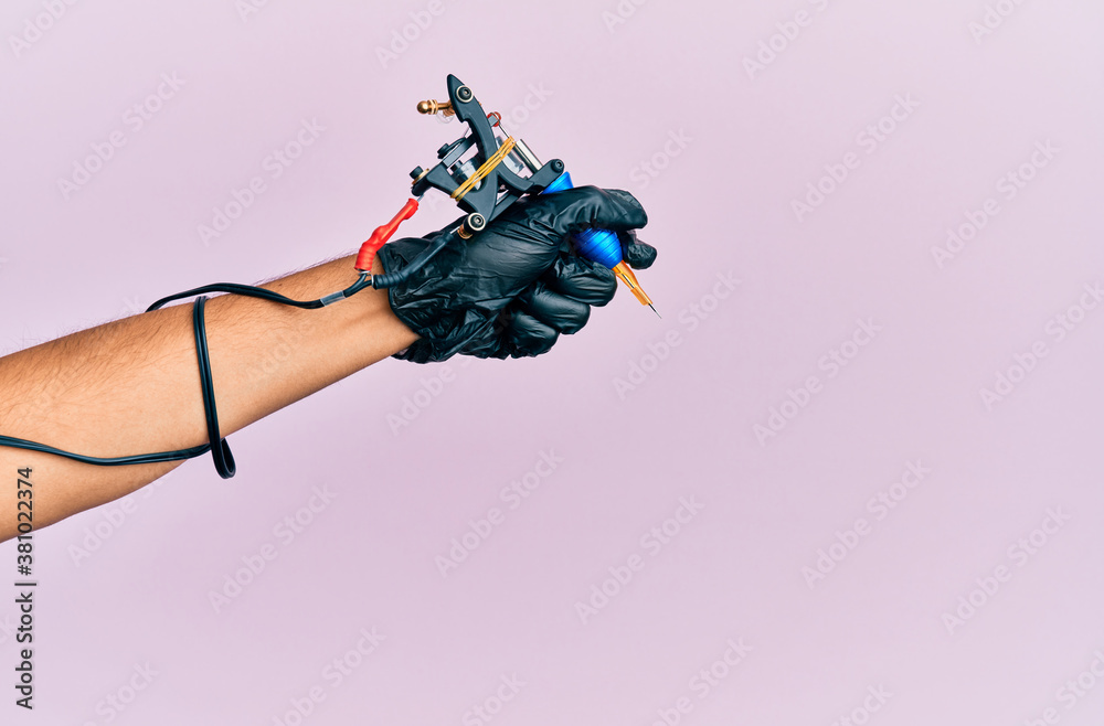 Obraz premium Hand of young hispanic man using tattoo machine over isolated pink background.