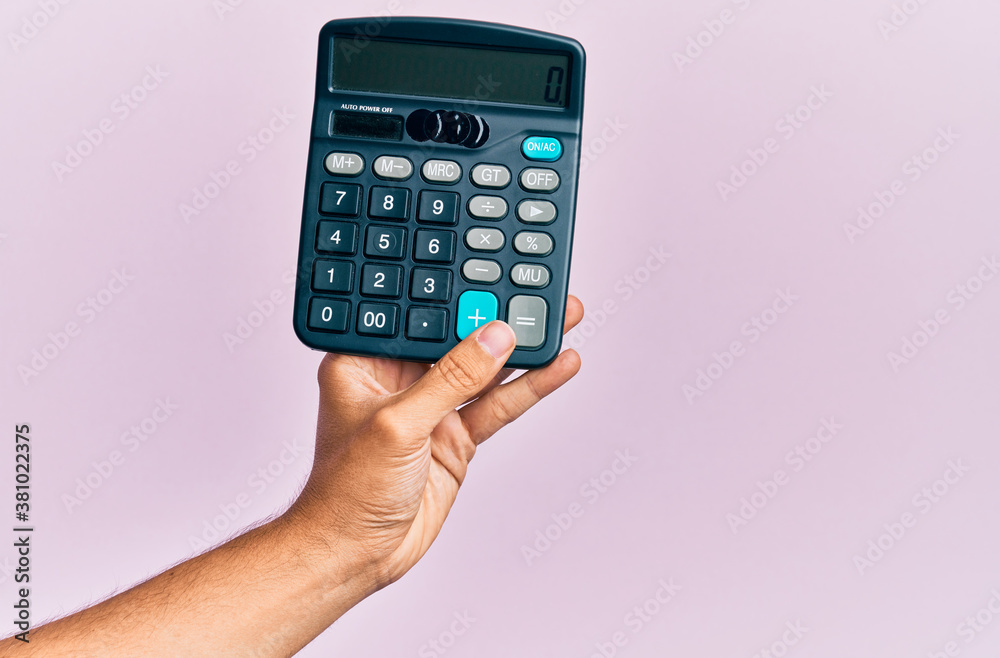 Hand of young hispanic man holding calculator over isolated pink background. Hand of young hispanic man holding calculator over isolated pink background.