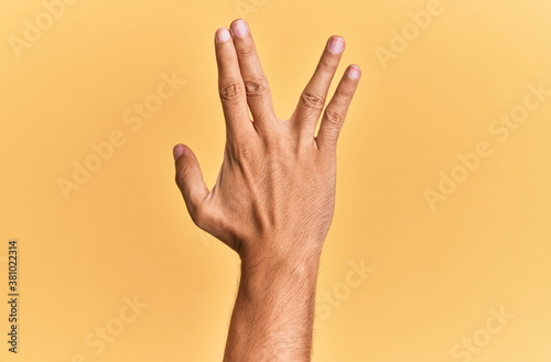 Arm and hand of caucasian man over yellow isolated background greeting doing vulcan salute  showing back of the hand and fingers  freak culture