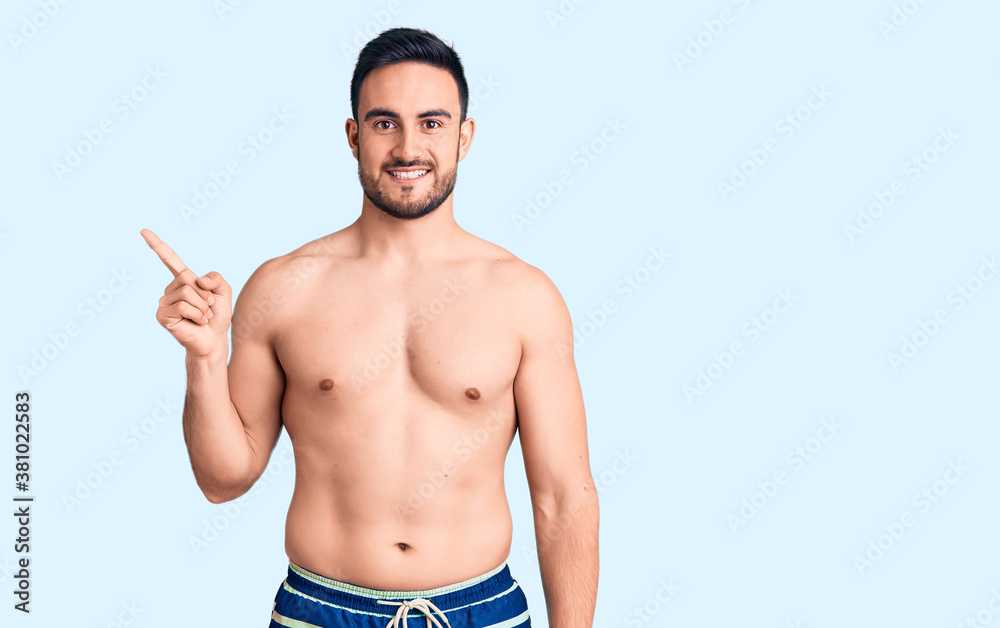 Young handsome man wearing swimwear with a big smile on face, pointing with hand finger to the side looking at the camera. Young handsome man wearing swimwear with a big smile on face, pointing with hand finger to the side looking at the camera.