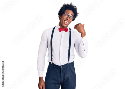 Handsome african american man with afro hair wearing hipster elegant look smiling with happy face looking and pointing to the side with thumb up.