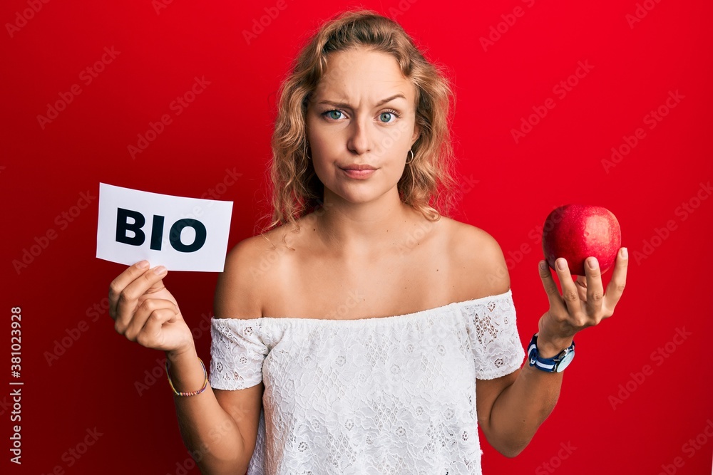 Beautiful caucasian woman holding red apple and bio word skeptic and nervous, frowning upset because of problem. negative person. Beautiful caucasian woman holding red apple and bio word skeptic and nervous, frowning upset because of problem. negative person.