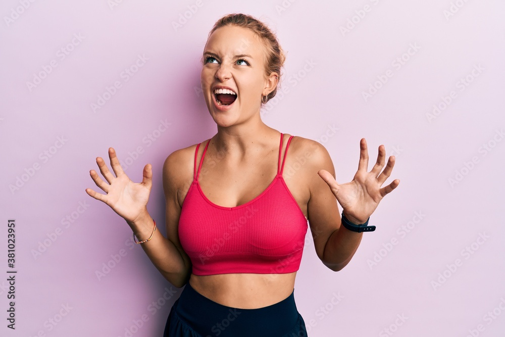 Beautiful caucasian woman wearing sportswear crazy and mad shouting and yelling with aggressive expression and arms raised. frustration concept. Beautiful caucasian woman wearing sportswear crazy and mad shouting and yelling with aggressive expression and arms raised. frustration concept.