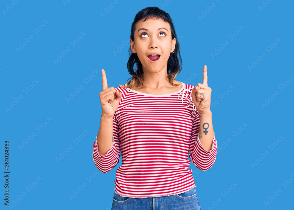 Young woman wearing casual clothes amazed and surprised looking up and pointing with fingers and raised arms. Young woman wearing casual clothes amazed and surprised looking up and pointing with fingers and raised arms.