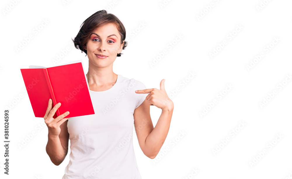 Beautiful young woman with short hair reading a book pointing finger to one self smiling happy and proud Beautiful young woman with short hair reading a book pointing finger to one self smiling happy and proud