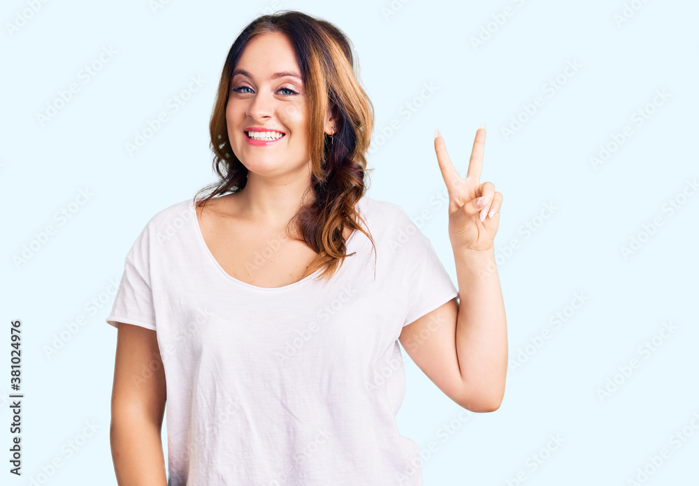 Young beautiful caucasian woman wearing casual white tshirt smiling looking to the camera showing fingers doing victory sign. number two. Young beautiful caucasian woman wearing casual white tshirt smiling looking to the camera showing fingers doing victory sign. number two.
