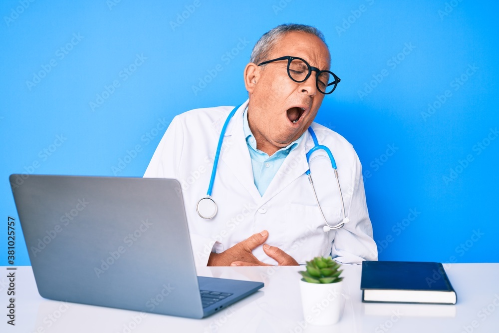 Senior handsome man with gray hair wearing doctor uniform working using computer laptop with hand on stomach because nausea, painful disease feeling unwell. ache concept.