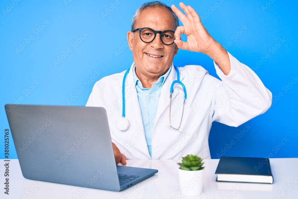 Senior handsome man with gray hair wearing doctor uniform working using computer laptop smiling positive doing ok sign with hand and fingers. successful expression. Senior handsome man with gray hair wearing doctor uniform working using computer laptop smiling positive doing ok sign with hand and fingers. successful expression.