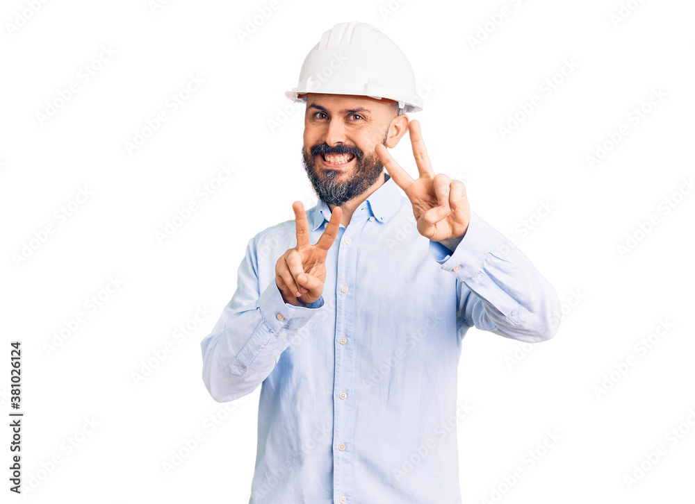 Young handsome man wearing architect hardhat smiling looking to the camera showing fingers doing victory sign. number two. Young handsome man wearing architect hardhat smiling looking to the camera showing fingers doing victory sign. number two.