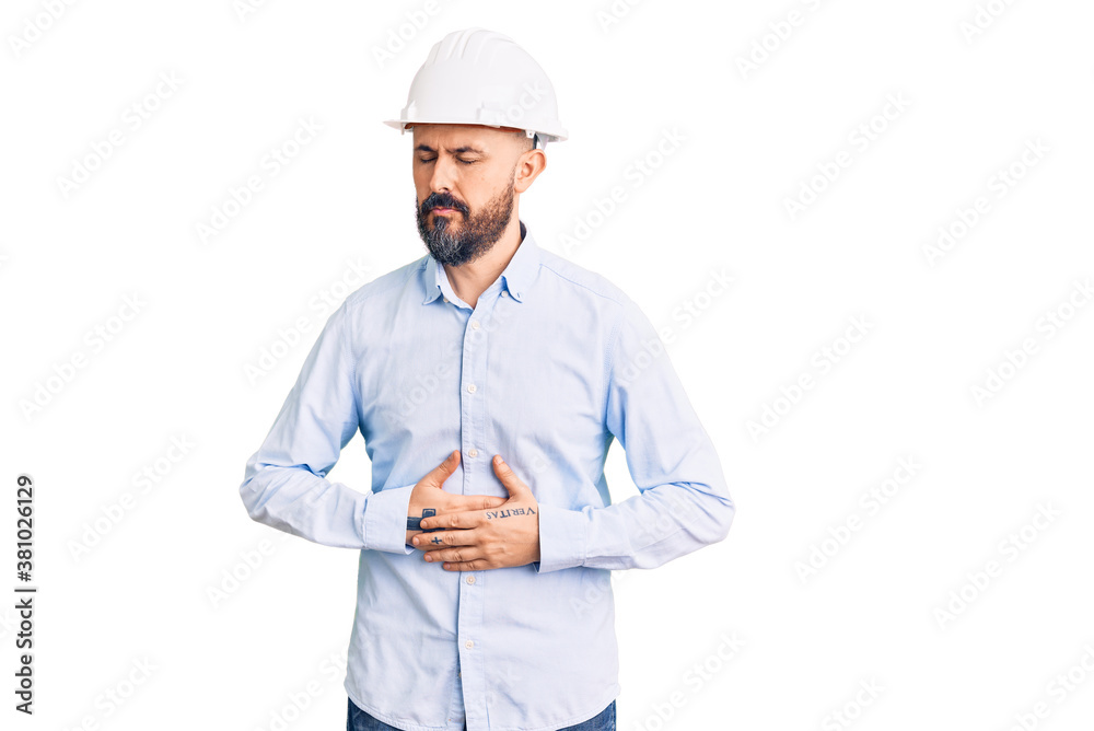 Young handsome man wearing architect hardhat with hand on stomach because indigestion, painful illness feeling unwell. ache concept. Young handsome man wearing architect hardhat with hand on stomach because indigestion, painful illness feeling unwell. ache concept.
