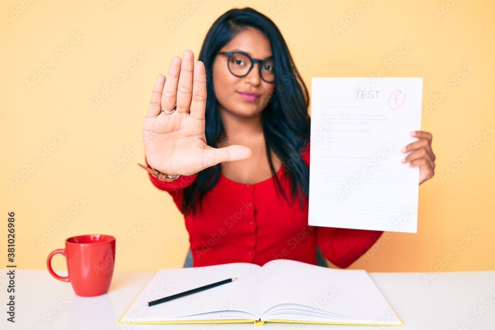 Beautiful latin young woman with long hair showing a failed exam with open hand doing stop sign with serious and confident expression, defense gesture