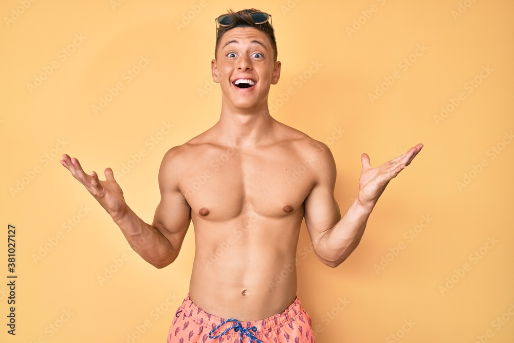 Young hispanic boy wearing swimwear shirtless celebrating victory with happy smile and winner expression with raised hands