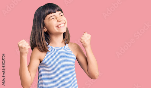 Young little girl with bang wearing casual clothes very happy and excited doing winner gesture with arms raised, smiling and screaming for success. celebration concept.