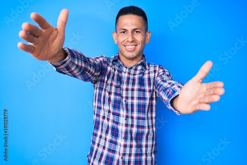 Young handsome latin man wearing casual clothes looking at the camera smiling with open arms for hug. cheerful expression embracing happiness.