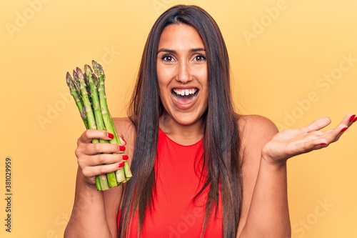 Young beautiful brunette woman holding asparagus celebrating achievement with happy smile and winner expression with raised hand