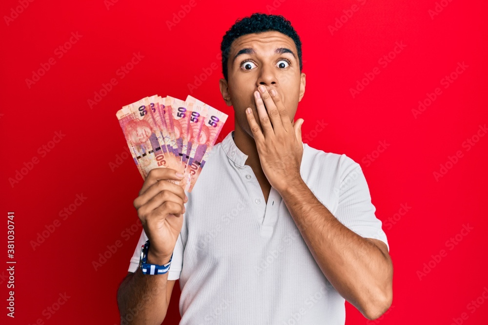 Young arab man holding south african rand banknotes covering mouth with hand, shocked and afraid for mistake. surprised expression Young arab man holding south african rand banknotes covering mouth with hand, shocked and afraid for mistake. surprised expression