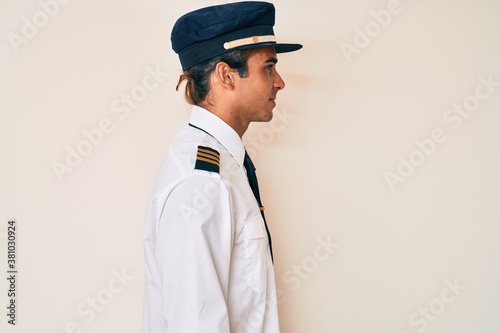 Young hispanic man wearing airplane pilot uniform looking to side, relax profile pose with natural face and confident smile. © Krakenimages.com