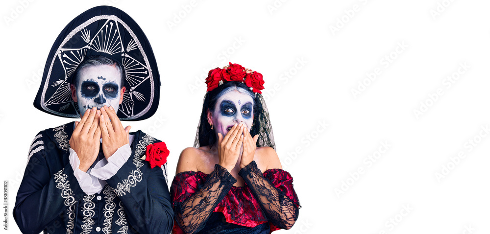 Young couple wearing mexican day of the dead costume over background laughing and embarrassed giggle covering mouth with hands, gossip and scandal concept