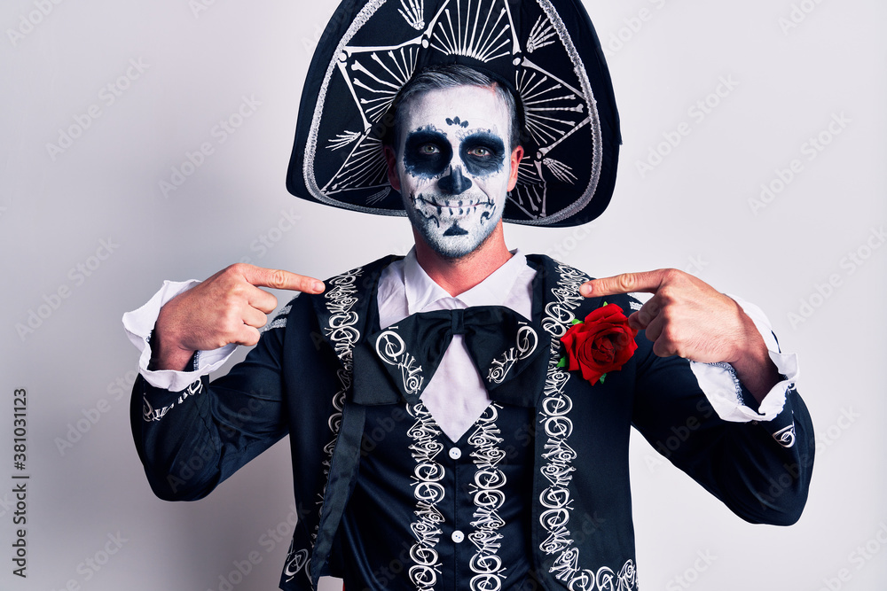 Young man wearing mexican day of the dead costume over white looking confident with smile on face, pointing oneself with fingers proud and happy.