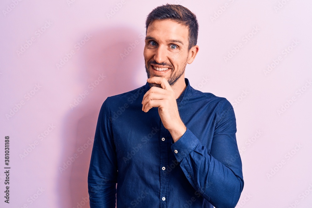 Young handsome man wearing casual shirt standing over isolated pink background smiling looking confident at the camera with crossed arms and hand on chin. Thinking positive.