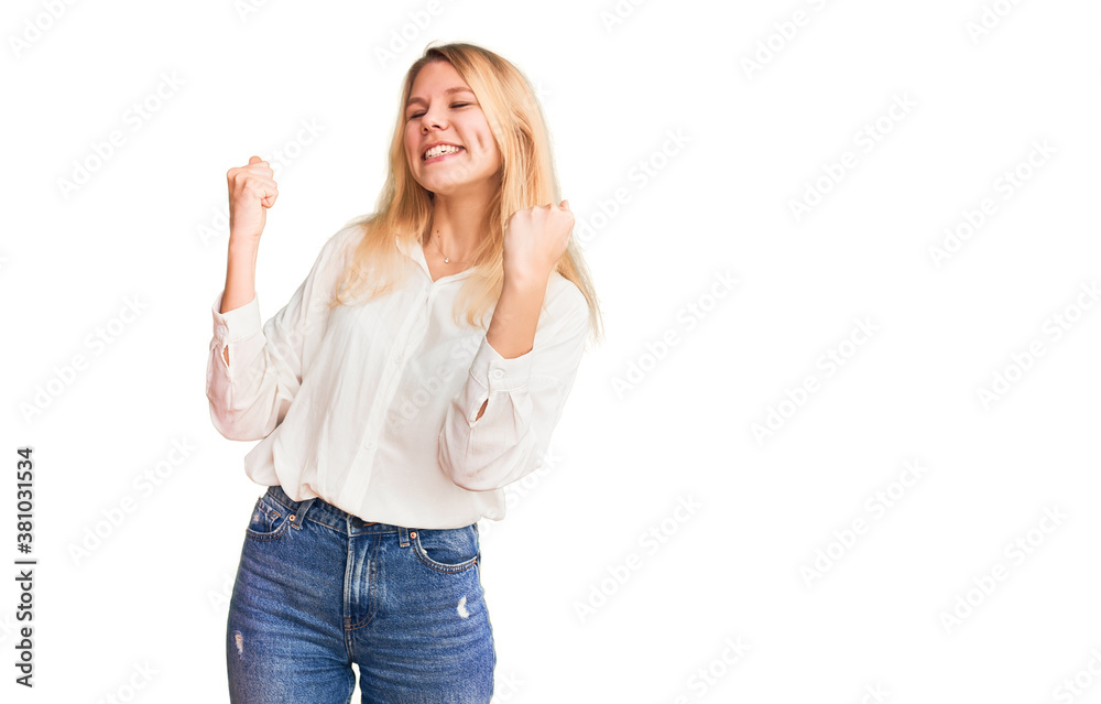Young beautiful blonde woman wearing casual shirt very happy and excited doing winner gesture with arms raised, smiling and screaming for success. celebration concept. Young beautiful blonde woman wearing casual shirt very happy and excited doing winner gesture with arms raised, smiling and screaming for success. celebration concept.