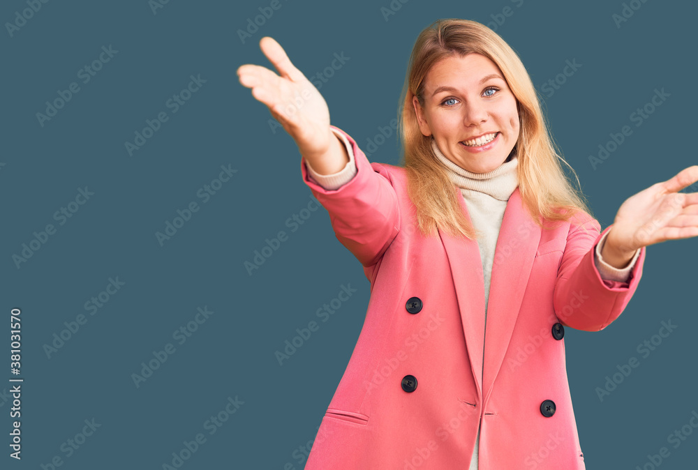 Young beautiful blonde woman wearing elegant clothes looking at the camera smiling with open arms for hug. cheerful expression embracing happiness. Young beautiful blonde woman wearing elegant clothes looking at the camera smiling with open arms for hug. cheerful expression embracing happiness.