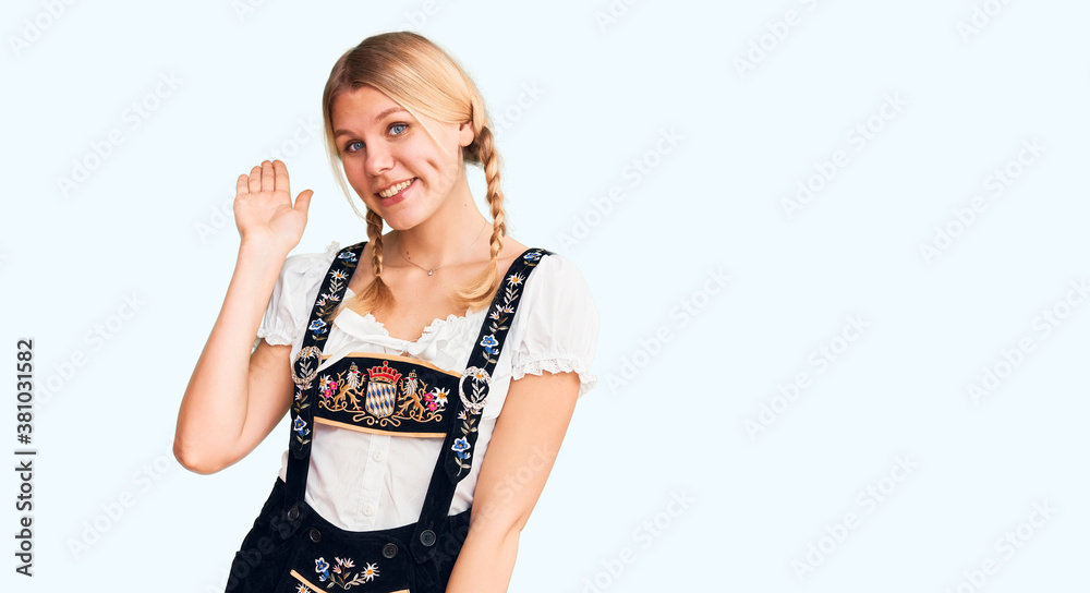 Young beautiful blonde woman wearing oktoberfest dress waiving saying hello happy and smiling, friendly welcome gesture Young beautiful blonde woman wearing oktoberfest dress waiving saying hello happy and smiling, friendly welcome gesture