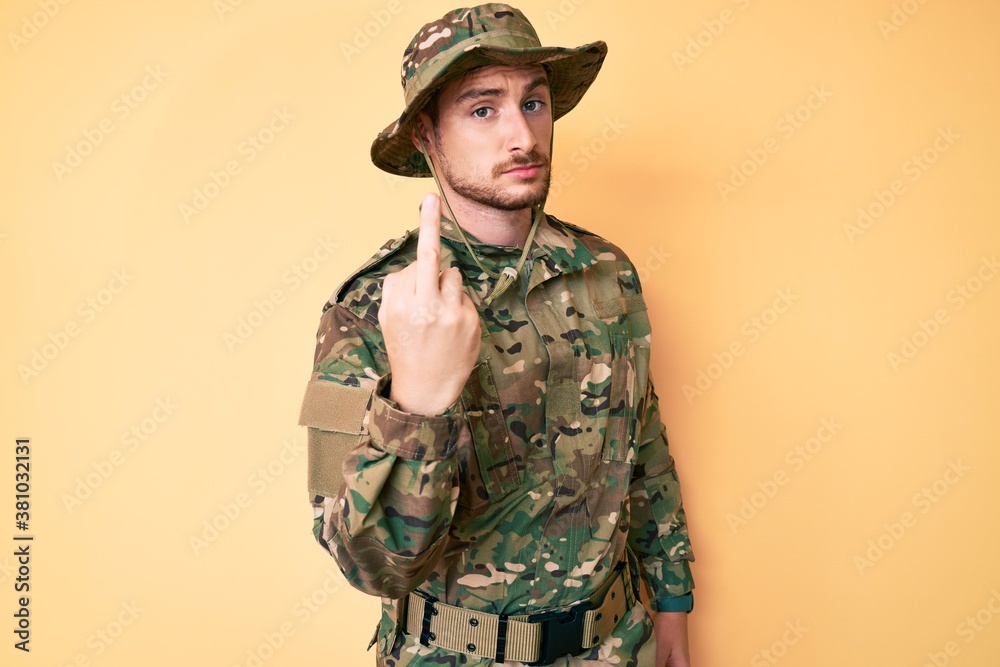 Young caucasian man wearing camouflage army uniform showing middle finger, impolite and rude fuck off expression