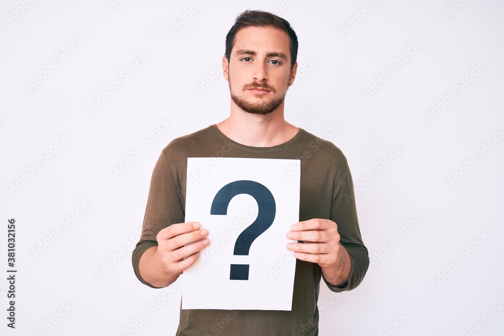 Young handsome man holding question mark thinking attitude and sober expression looking self confident Young handsome man holding question mark thinking attitude and sober expression looking self confident