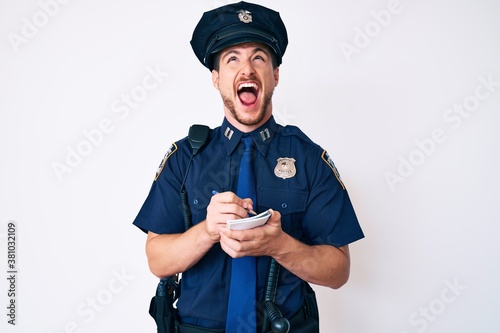 Young caucasian man wearing police uniform writing fine angry and mad screaming frustrated and furious, shouting with anger looking up.