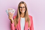 Young blonde woman wearing business style holding mexican pesos looking positive and happy standing and smiling with a confident smile showing teeth