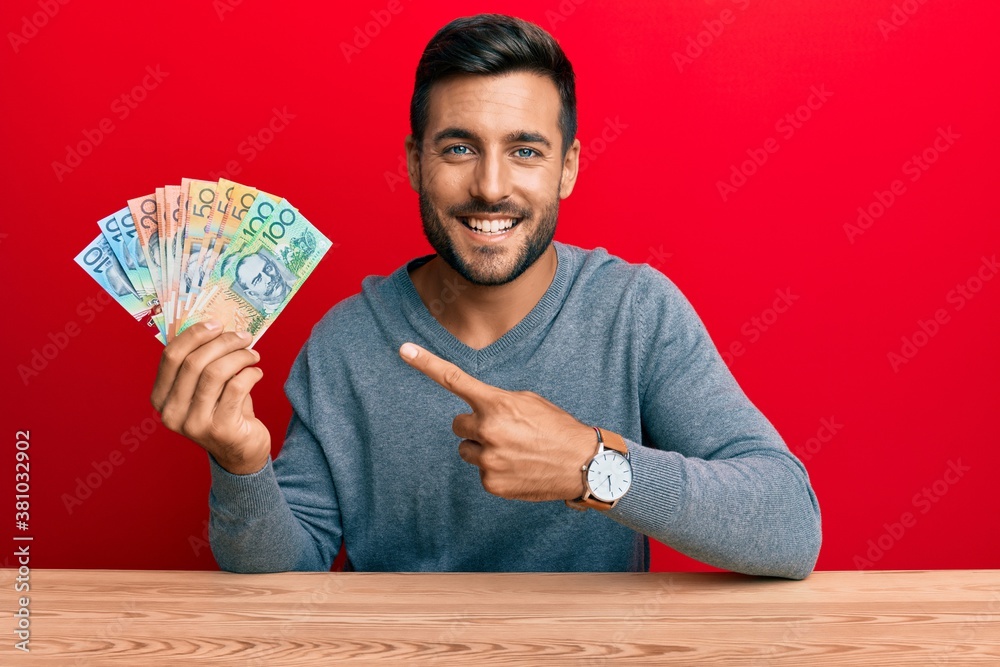 Handsome hispanic man holding australian dollars smiling happy pointing with hand and finger Handsome hispanic man holding australian dollars smiling happy pointing with hand and finger