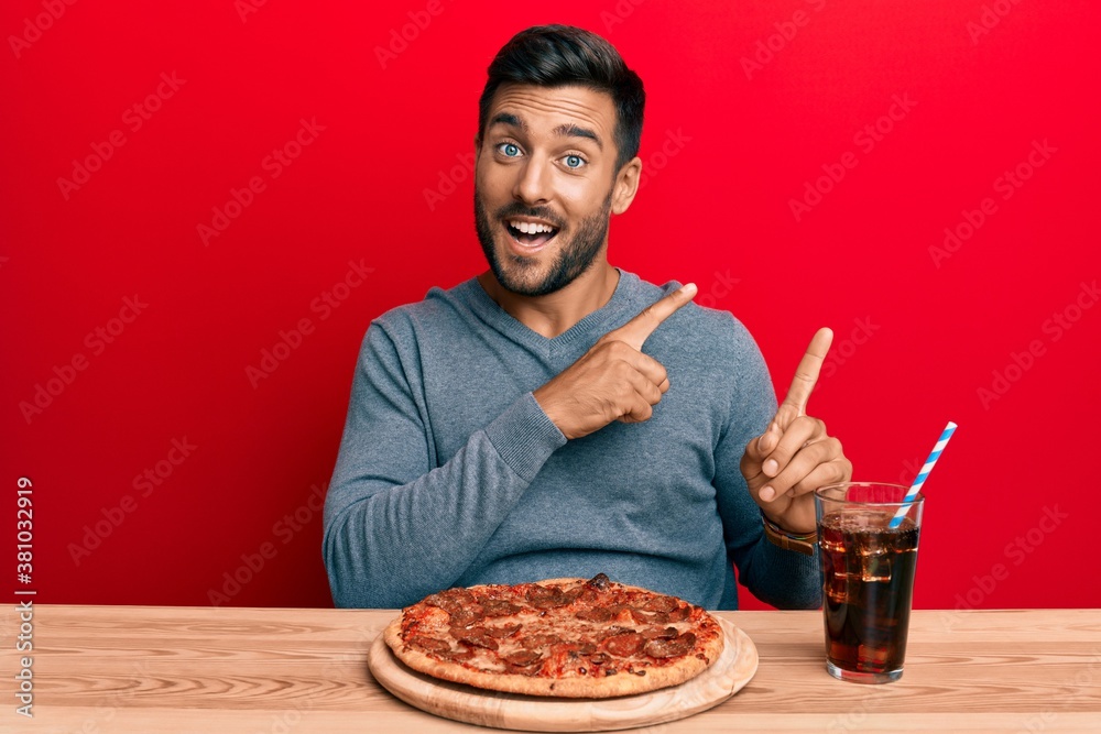 Handsome hispanic man eating tasty pepperoni pizza smiling and looking