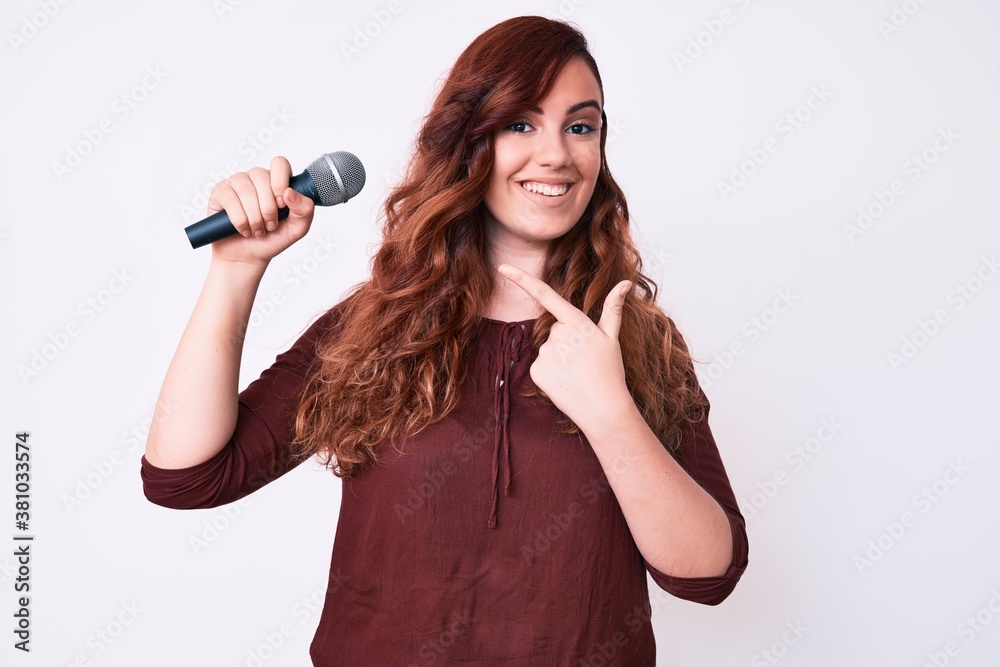 Young beautiful woman singing song using microphone smiling happy pointing with hand and finger Young beautiful woman singing song using microphone smiling happy pointing with hand and finger