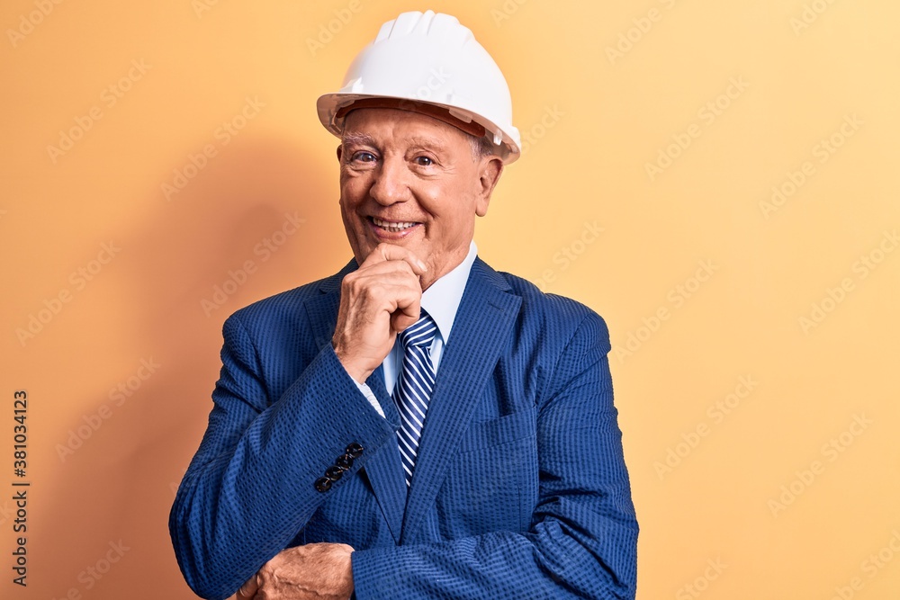 Senior grey-haired architect man wearing suit and security hardhat over yellow background smiling looking confident at the camera with crossed arms and hand on chin. Thinking positive. Senior grey-haired architect man wearing suit and security hardhat over yellow background smiling looking confident at the camera with crossed arms and hand on chin. Thinking positive.