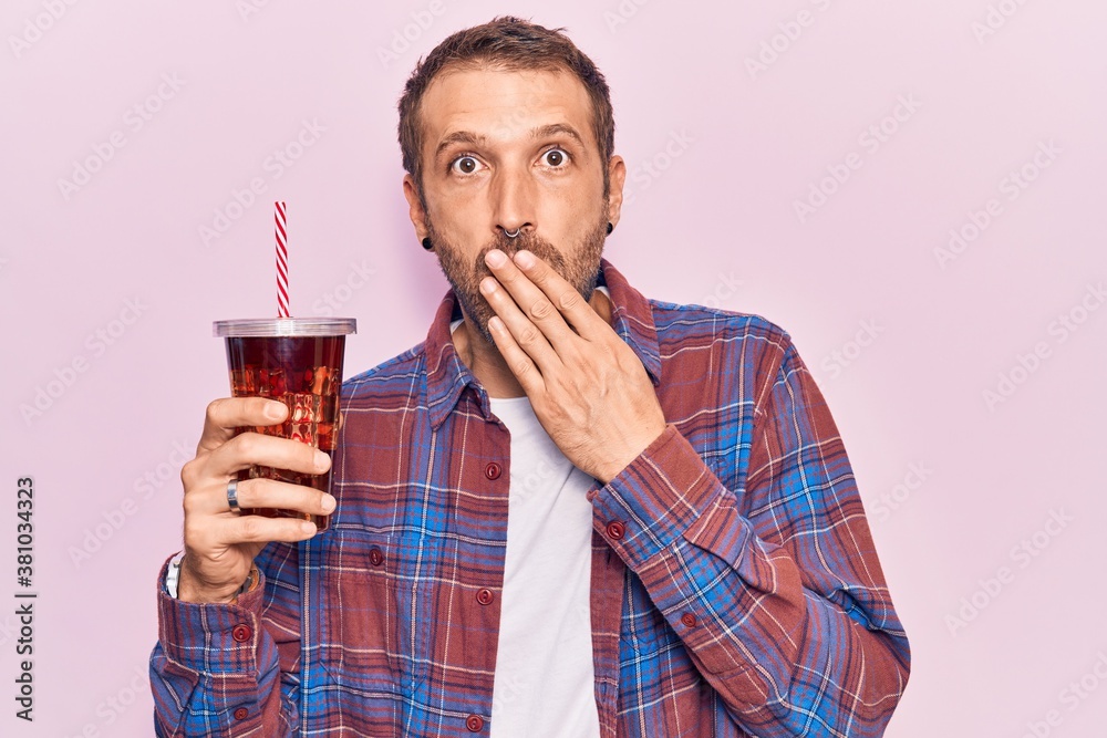 Young handsome man drinking glass of cola beverage covering mouth with hand, shocked and afraid for mistake. surprised expression Young handsome man drinking glass of cola beverage covering mouth with hand, shocked and afraid for mistake. surprised expression