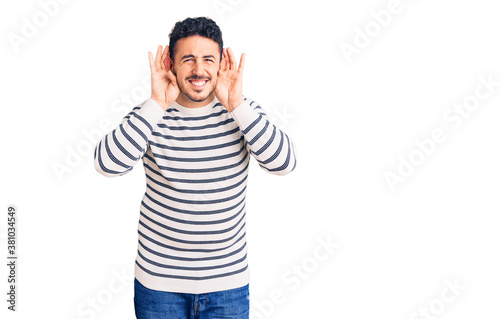 Young hispanic man wearing casual clothes trying to hear both hands on ear gesture, curious for gossip. hearing problem, deaf