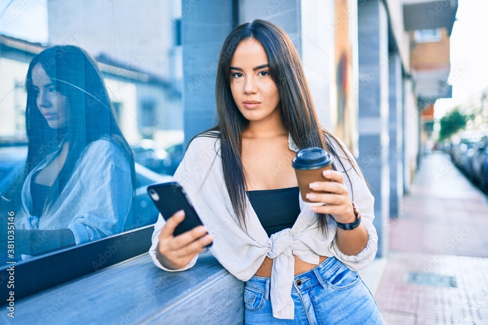Young hispanic girl  with serious expression using smartphone and drinking take away coffee at the city.