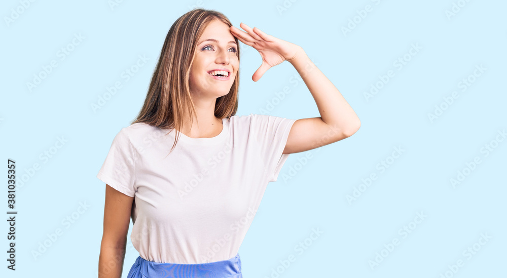 Young beautiful blonde woman wearing summer style very happy and smiling looking far away with hand over head. searching concept. Young beautiful blonde woman wearing summer style very happy and smiling looking far away with hand over head. searching concept.