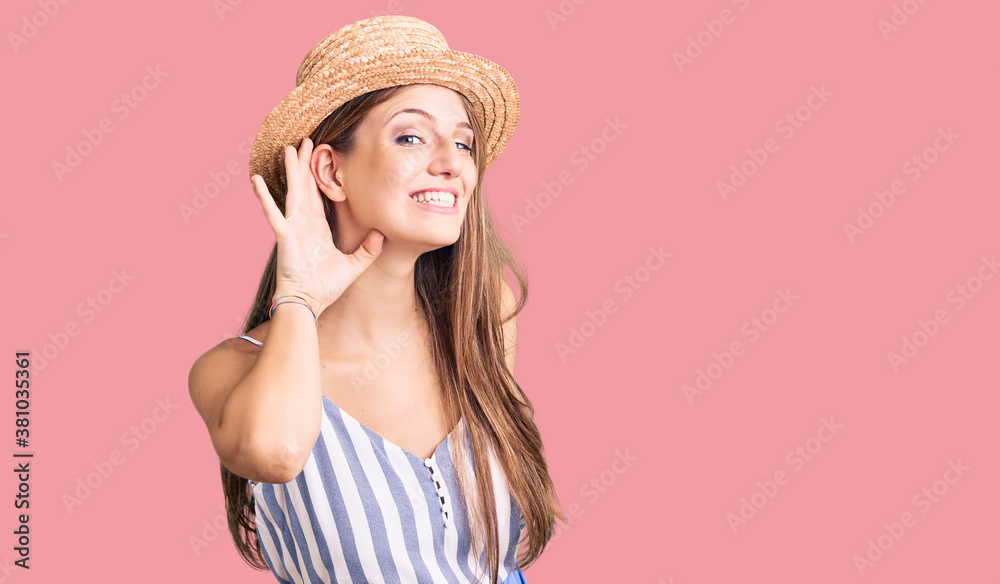 Young beautiful blonde woman wearing summer hat smiling with hand over ear listening an hearing to rumor or gossip. deafness concept. Young beautiful blonde woman wearing summer hat smiling with hand over ear listening an hearing to rumor or gossip. deafness concept.