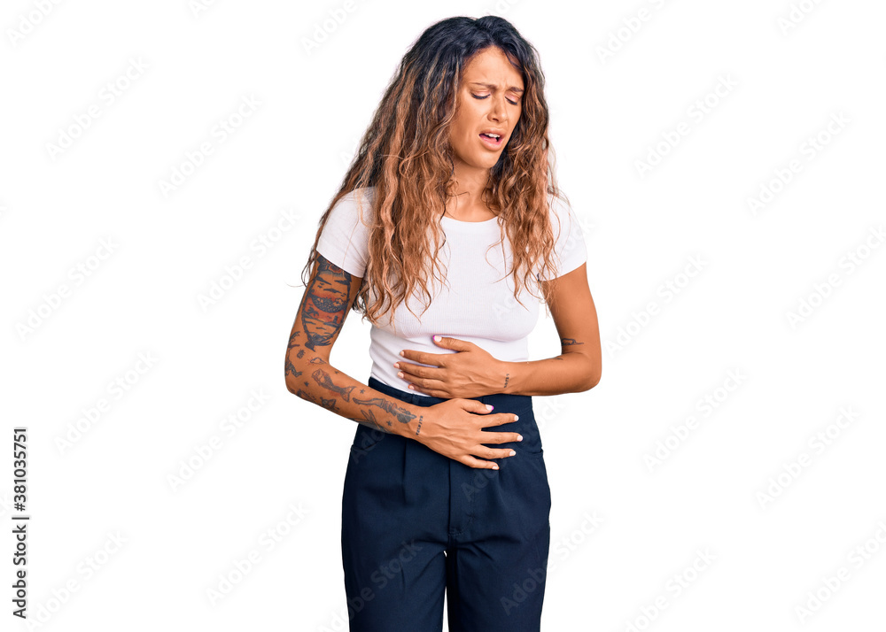 Young hispanic woman with tattoo wearing casual white tshirt with hand on stomach because nausea, painful disease feeling unwell. ache concept. Young hispanic woman with tattoo wearing casual white tshirt with hand on stomach because nausea, painful disease feeling unwell. ache concept.
