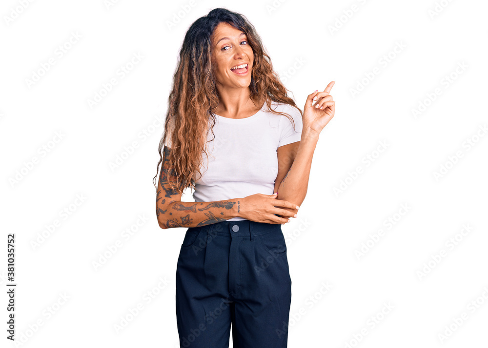 Young hispanic woman with tattoo wearing casual white tshirt with a big smile on face, pointing with hand and finger to the side looking at the camera. Young hispanic woman with tattoo wearing casual white tshirt with a big smile on face, pointing with hand and finger to the side looking at the camera.